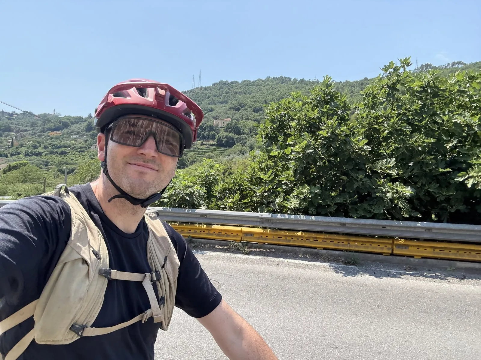 Brian in his bike helmet and riding glasses, with green hills behind him